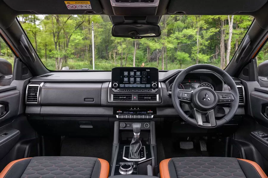 O interior renovado da L200 apresenta um design moderno, com um painel redesenhado, um volante multifuncional e uma central multimídia flutuante, oferecendo conectividade avançada e conforto para os ocupantes.