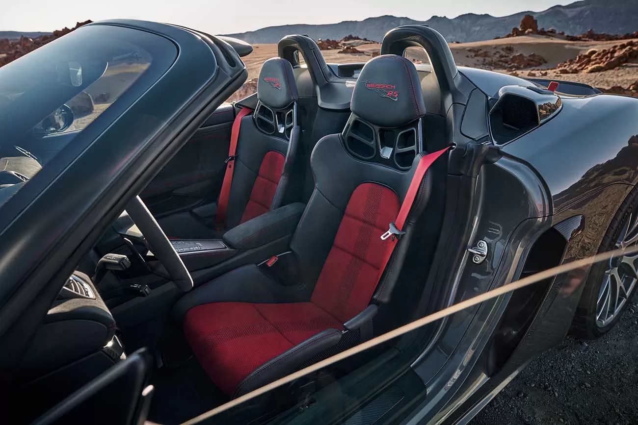 O interior do Porsche 718 Spyder RS combina luxo e esportividade, com assentos tipo concha revestidos em Race-Tex e um volante esportivo revestido em couro de alta qualidade, proporcionando conforto e suporte superiores em todas as viagens.